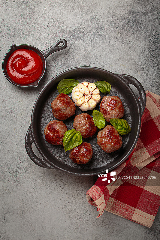 俯视视角拍摄的美味自制肉丸，配以新鲜罗勒和蒜，装在小锅中，佐以番茄酱，摆放在乡村风格的桌面上，准备享用图片素材
