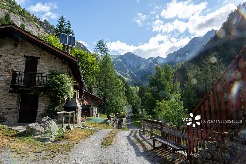 山谷中的石头小屋，配有太阳能电池板和蜿蜒的土路，背景是蓝天，意大利，库马约尔图片素材