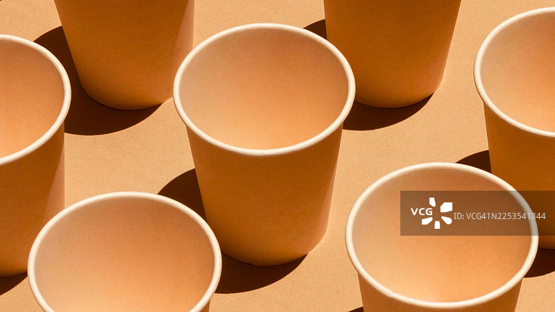 俯视角度拍摄的多个空的一次性杯子，背景为棕色，杯子投下阴影图片素材