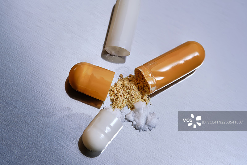 特写镜头，一颗打开的药丸，里面的粉末洒落在金属表面，象征着医药和健康图片素材