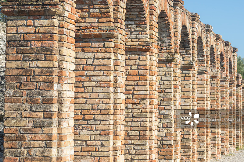 仰视镜头拍摄的古老风化砖墙，带有拱门，背景是晴朗的蓝天，意大利，历史与坚韧的象征图片素材