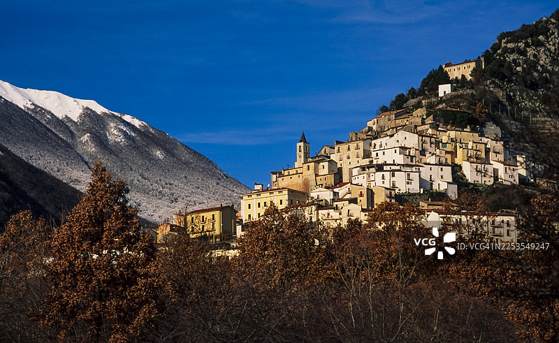 坐落在山坡上的历史悠久的村庄，背景是白雪皑皑的山峰和湛蓝的天空，意大利图片素材