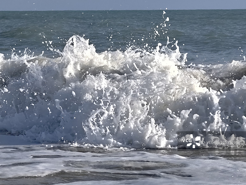 晴空下的汹涌海浪，白色浪花和飞溅的水珠，充满动感的特写图片素材
