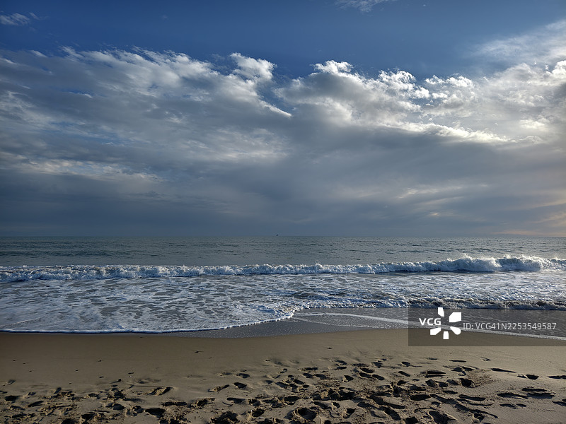 日落时分，壮阔多云的天空下，宁静海滩的风景，伴随着轻柔的海浪图片素材