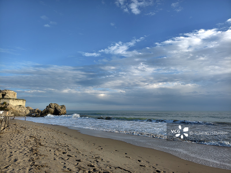 海边沙滩的风景，海浪拍打着，天空是深邃的蓝色，点缀着云彩。图片素材