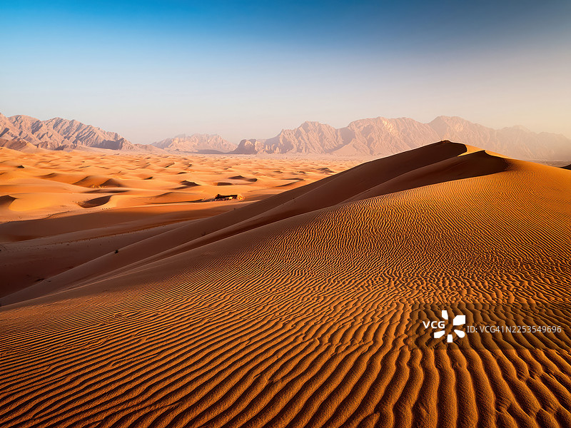 阿曼瓦希巴沙漠，日出时分，晴朗天空下的雄伟沙漠沙丘和山脉图片素材