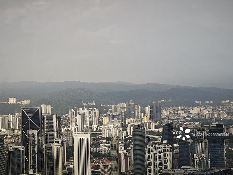 从高处俯瞰马来西亚城市景观，远方是连绵的山脉和多云的天空。图片素材