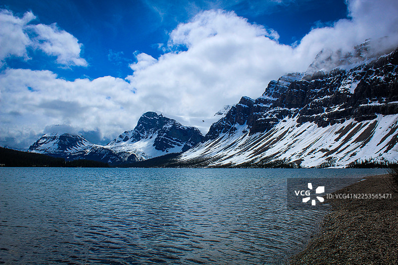 加拿大卡尔加里班夫国家公园，庄严的雪山倒映在宁静的湖水中，戏剧性的蓝天白云展现了大自然的壮丽之美图片素材