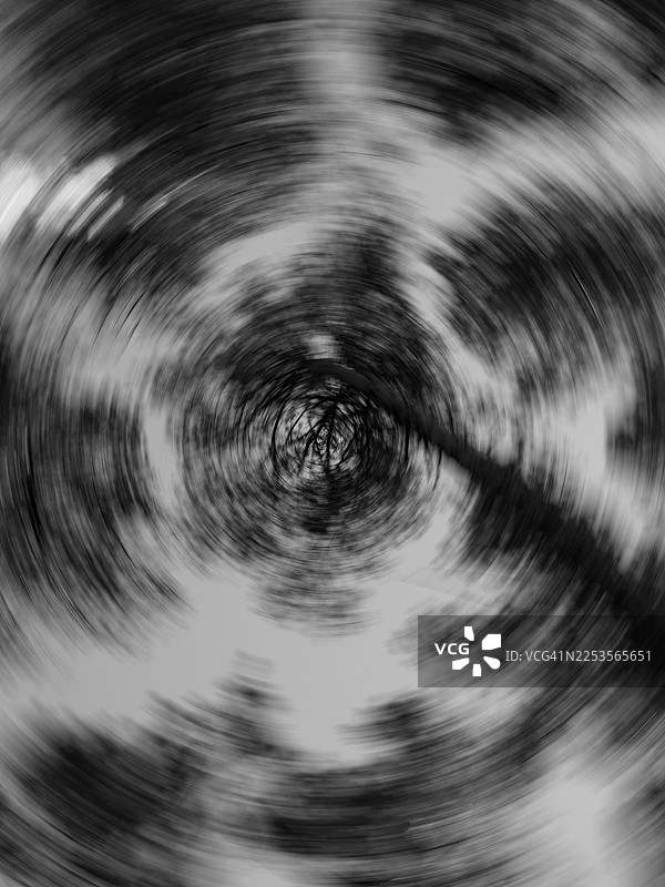 向上仰视的树干和树枝产生的圆形运动模糊，围绕黑暗的中心形成螺旋图案。森林树冠以黑白渲染，具有强烈的径向运动、抽象纹理和柔和的色调过渡。图片素材