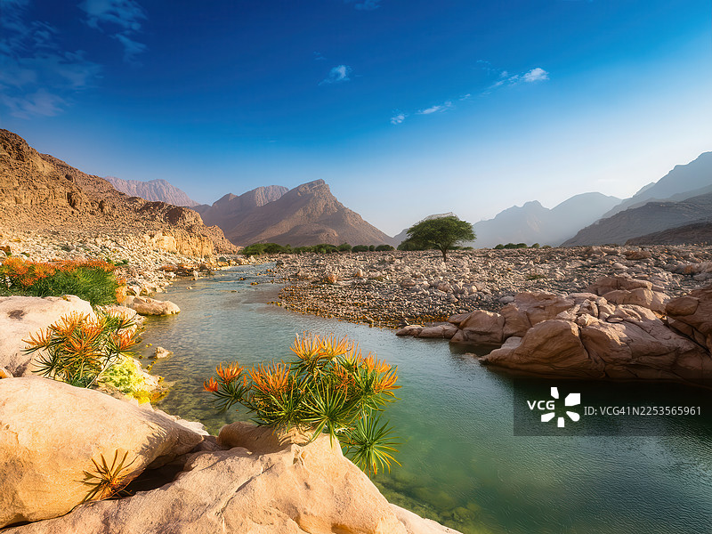阿曼塞拉莱，蓝天下，宁静的沙漠河谷，清澈的溪流穿过岩石地形和山脉图片素材