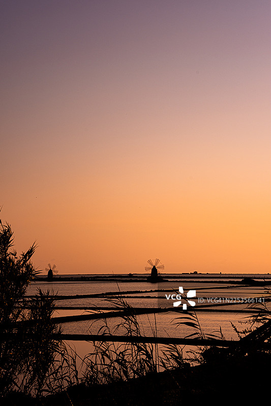 意大利马尔萨拉，盐田和风车在充满活力的日落天空中投下剪影的风景图片素材