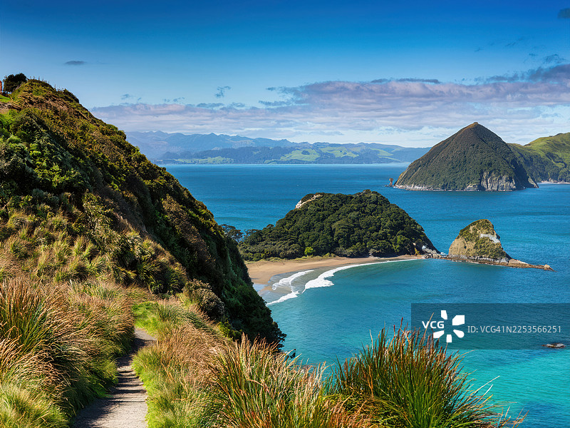 新西兰猴子岛令人惊叹的海岸风光，有蜿蜒的小路、郁郁葱葱的绿 hills 和碧绿的海洋，远处是岛屿，天空湛蓝图片素材