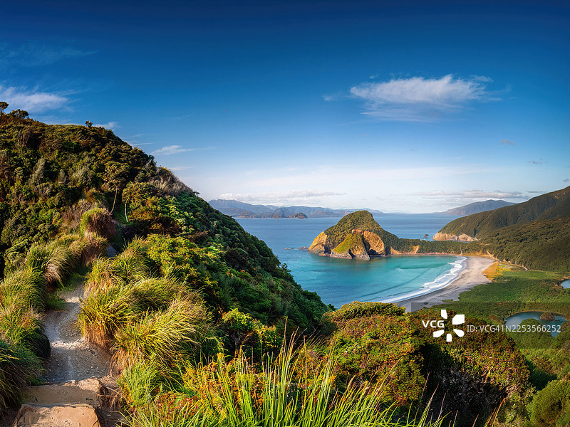 新西兰猴子岛，蔚蓝天空下，风景如画的海岸风光，蜿蜒小路俯瞰宁静海湾和葱郁山峦图片素材