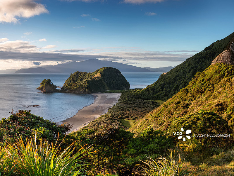新西兰猴子岛令人惊叹的海滨风景，有僻静的海滩、郁郁葱葱的绿山和远处的山脉，天空晴朗图片素材