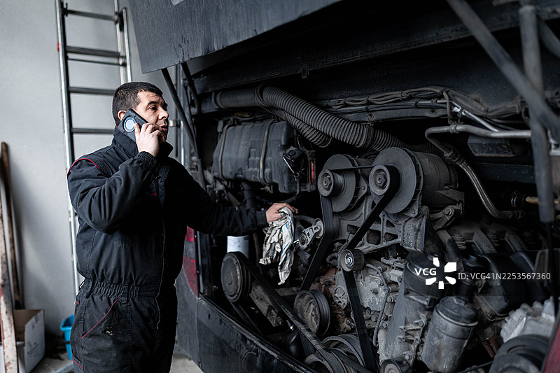 汽车维修工在维修重型车辆时使用手机图片素材