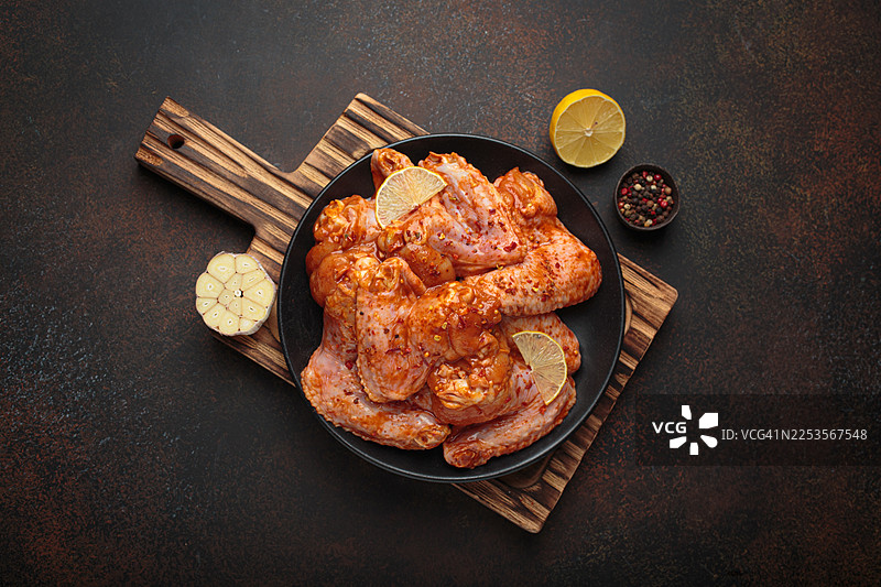 未煮的腌制鸡翅，配有香料、大蒜和柠檬，放在深色背景上，准备烹饪图片素材