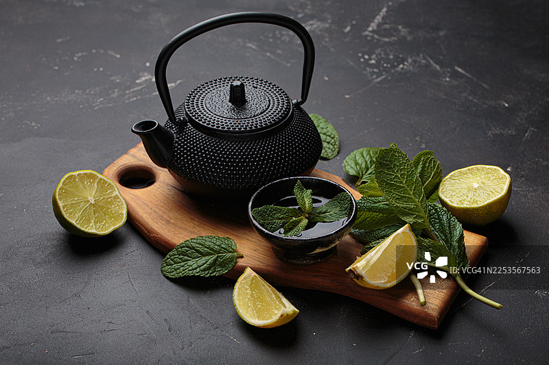 深色背景上，带有新鲜薄荷和柑橘的传统铸铁茶壶图片素材