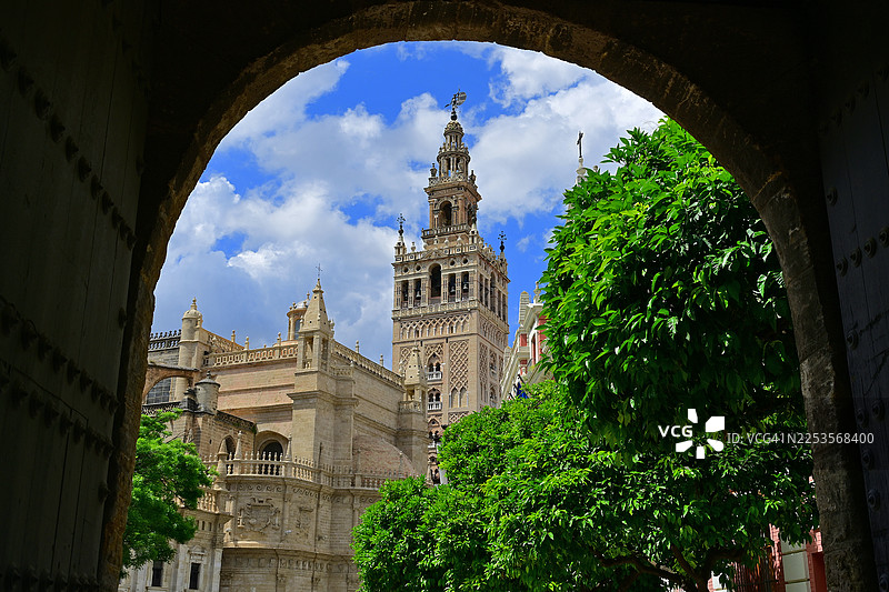 从拱门视角仰视吉拉尔达钟楼和塞维利亚大教堂，背景是带有云彩的蓝天，西班牙塞维利亚图片素材