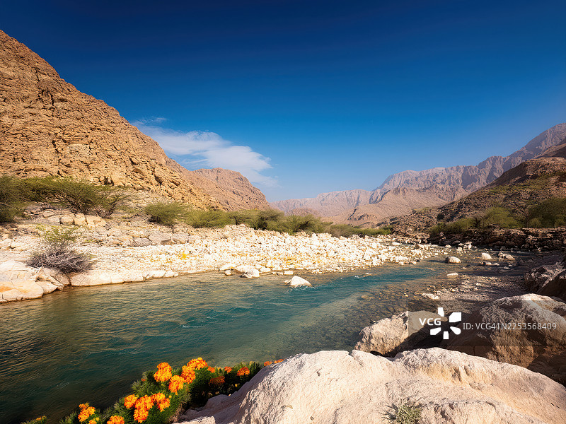中东干谷的风景，天空湛蓝，有岩石山脉和流淌的河流，地点：阿曼塞拉莱图片素材
