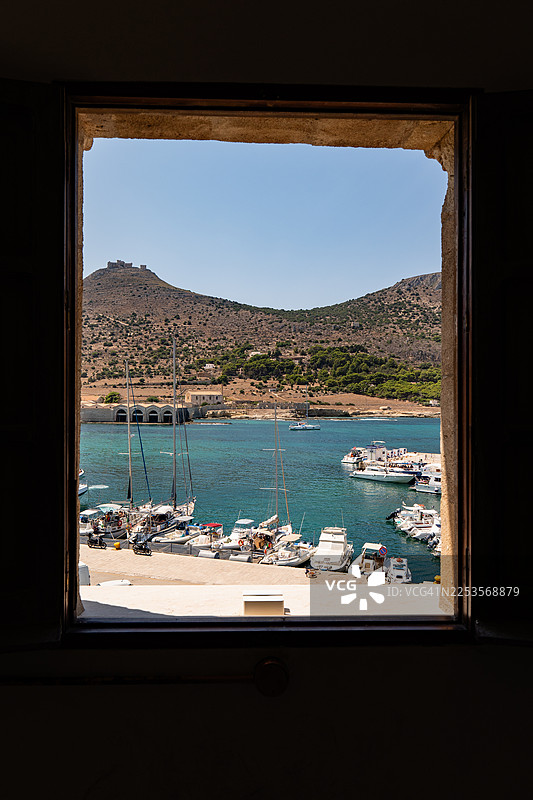 意大利埃加迪群岛，透过老旧的窗户望出去，可以看到船只和山脉点缀的繁华港口美景图片素材