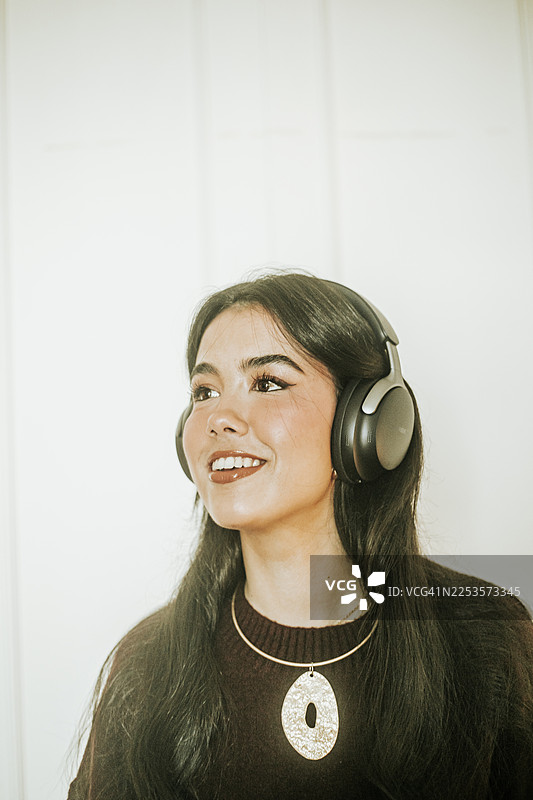一位年轻女子戴着银色包耳式耳机，微笑着看向镜头外。图片素材