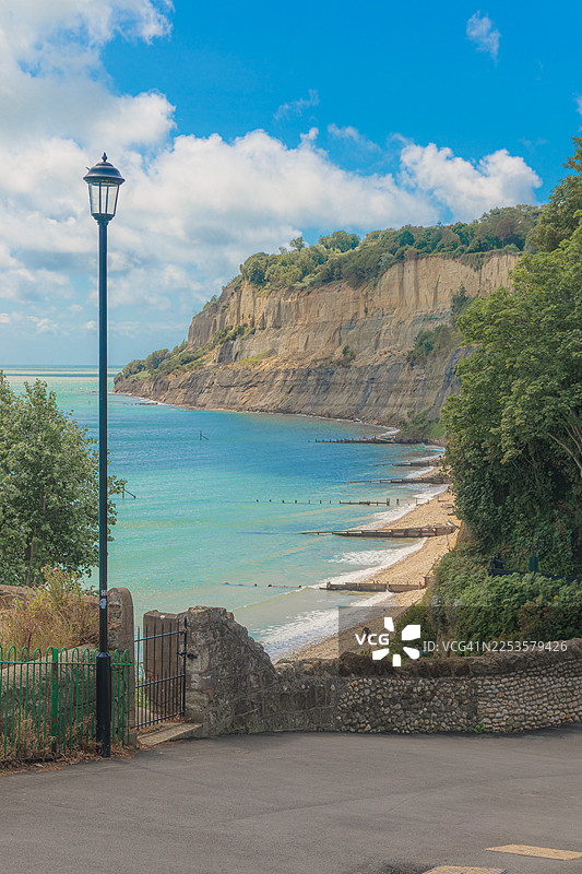 英国尚克林，蓝天白云下，宁静的海与崎岖的悬崖相接，前景中有灯柱和栅栏的风景图片素材