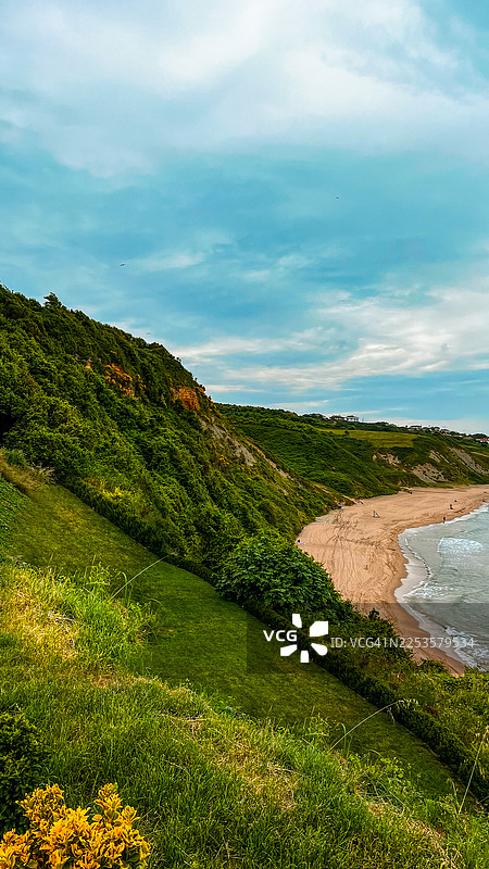 生机勃勃的绿色海岸悬崖和沙滩，映衬着动态的天空图片素材