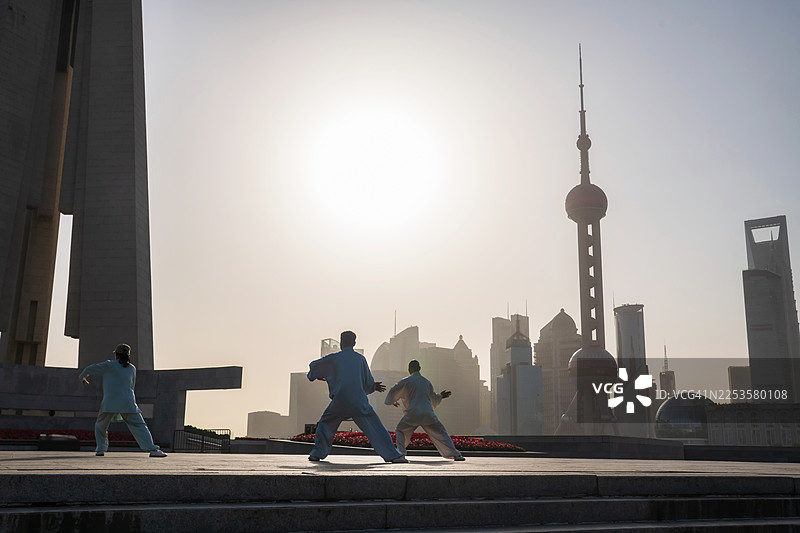 日出时分，现代都市中人们练习太极拳，剪影映衬着明亮的天空图片素材