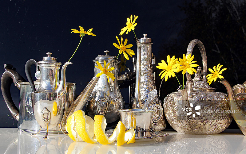 优雅的银色茶壶和茶杯，点缀着鲜艳的黄花和柠檬皮图片素材