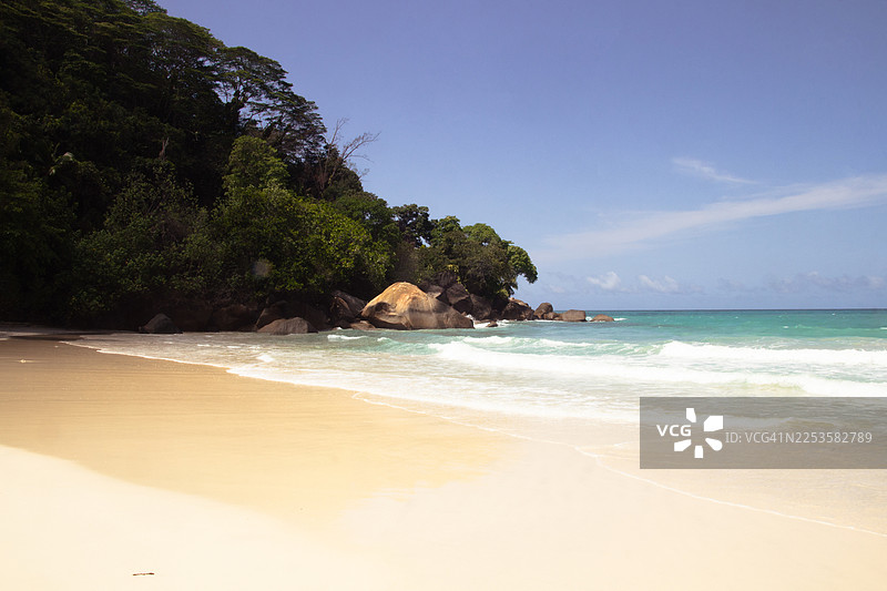 宁静的热带海滩，拥有郁郁葱葱的绿色山丘和碧绿的海浪，天空湛蓝，塞舌尔，马埃岛图片素材