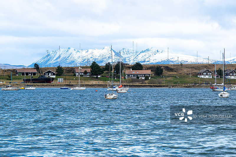 阿根廷乌斯怀亚的风景，可以看到宁静的海面、船只、房屋、雪山和多云的天空，地点为乌斯怀亚，阿根廷，预算阿根廷乌斯怀亚机场图片素材