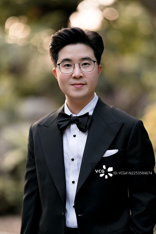 一位沉思的新郎在婚礼当天，在花园里望向别处。图片素材