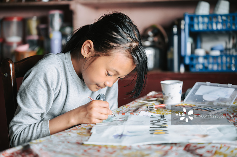一个年轻女孩在室内桌子前专注地在纸上绘画图片素材