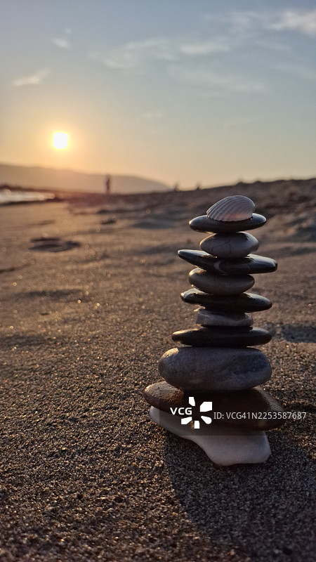 日落时分沙滩上堆叠的平衡石子和贝壳的特写，营造出平和宁静的氛围图片素材