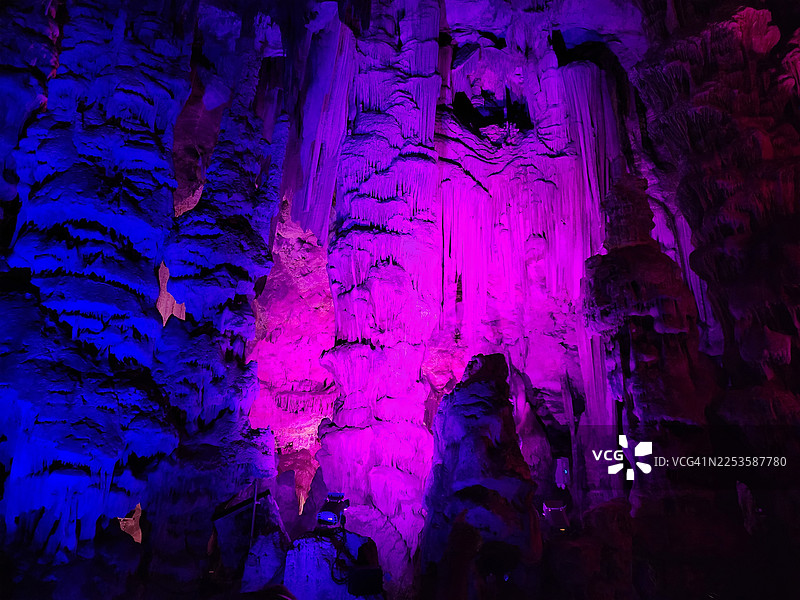 从低角度拍摄的洞穴，钟乳石和石笋在鲜艳的蓝紫色灯光下发光图片素材