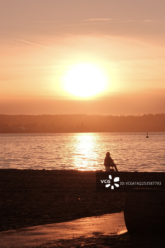 日落时分，沙滩上一个人的剪影，金色的光芒映照在水面上图片素材