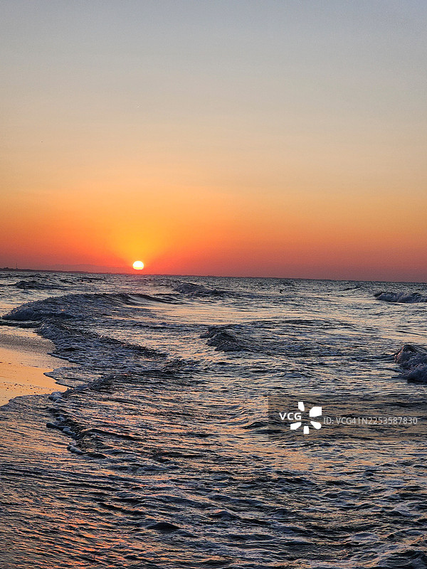 金色日落映照下的海洋，温和的海浪拍打着海岸，营造出宁静而如画般的自然景象图片素材