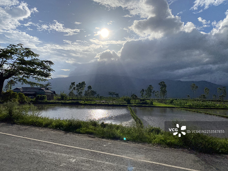 阳光穿破云层，洒在宁静的稻田和远处的山峦上图片素材