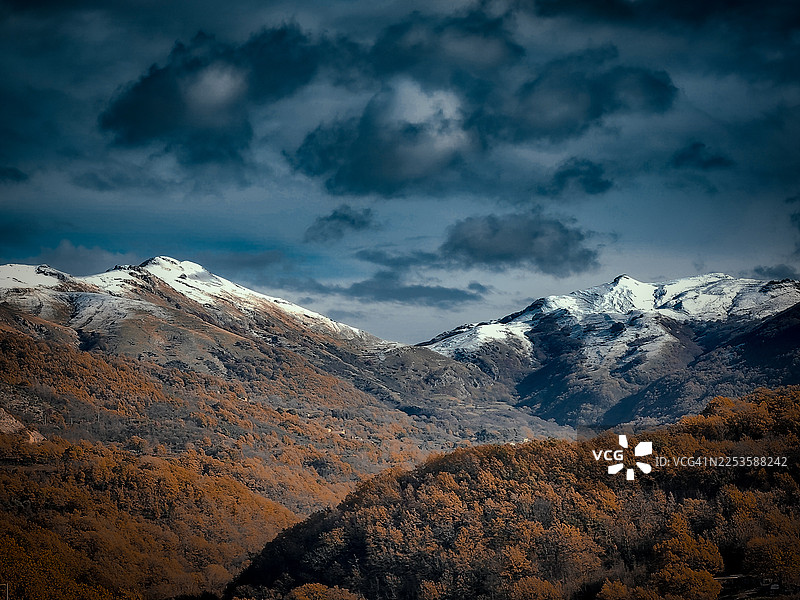 秋季森林与皑皑雪山在戏剧性天空下的风景图片素材