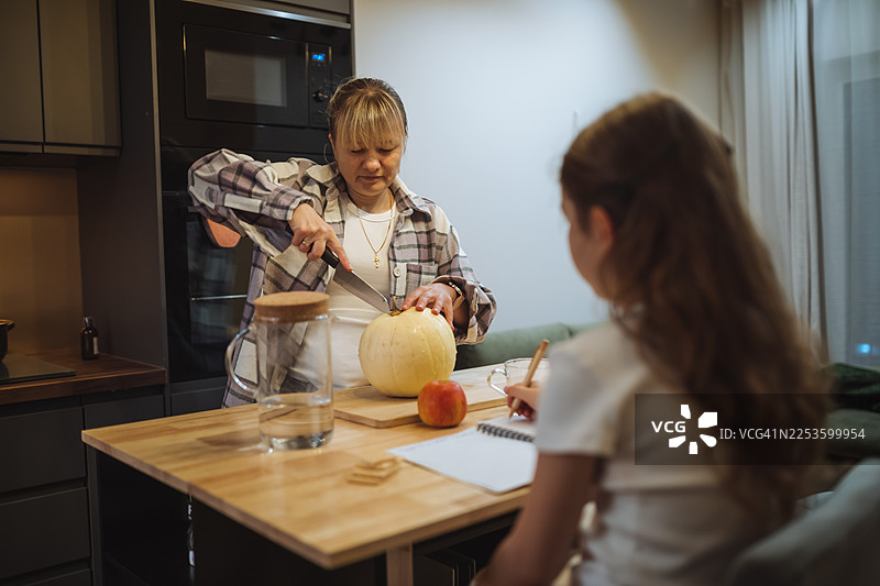 祖母在现代厨房准备水果，孙女在桌边画画，家中温馨的家庭时刻，舒适的居家氛围和自然的晚间光线图片素材