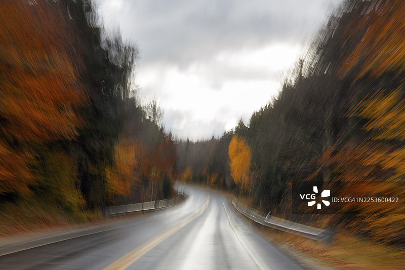 蜿蜒潮湿的乡村公路穿过森林，秋叶，印第安夏日，乌云，晕染效果，模糊，象征性照片，速度，坎卡马格斯公路，白山，新罕布什尔州，新英格兰，美国图片素材