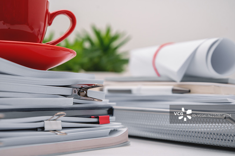 办公桌上放着白色的办公文具，上面有一个红色的咖啡杯。充满许多文件和空白笔记本的办公室氛围。图片素材