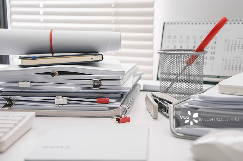 办公桌上的白色文具。堆积如山的纸张营造出办公氛围。空白记事本。图片素材