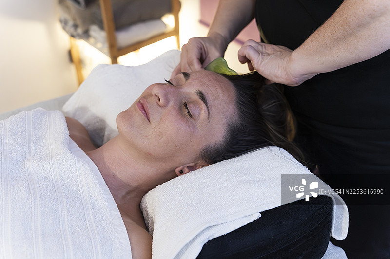 水疗沙龙里一位女士正在接受刮痧面部按摩图片素材