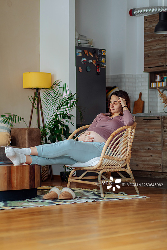 一位孕妇在家中的椅子上放松，浏览着她的笔记本电脑图片素材