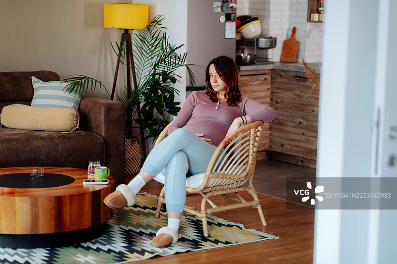 一位孕妇在家放松地坐在柳条椅上，抚摸着肚子图片素材