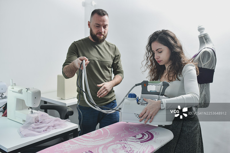 时装设计师和裁缝在工作室里用熨斗、布料和缝纫机工作图片素材