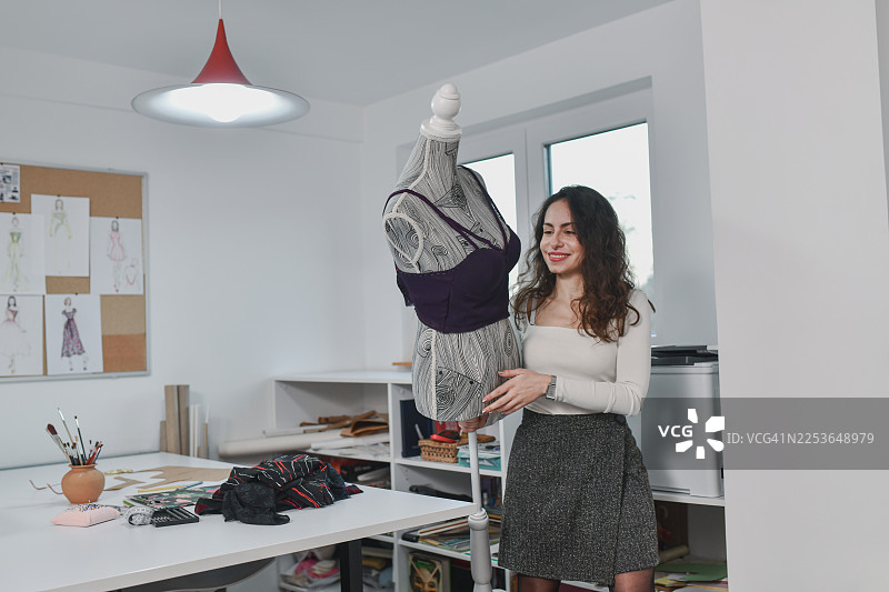 时尚设计师在现代工作室里使用带紫色上衣的服装模特进行工作图片素材