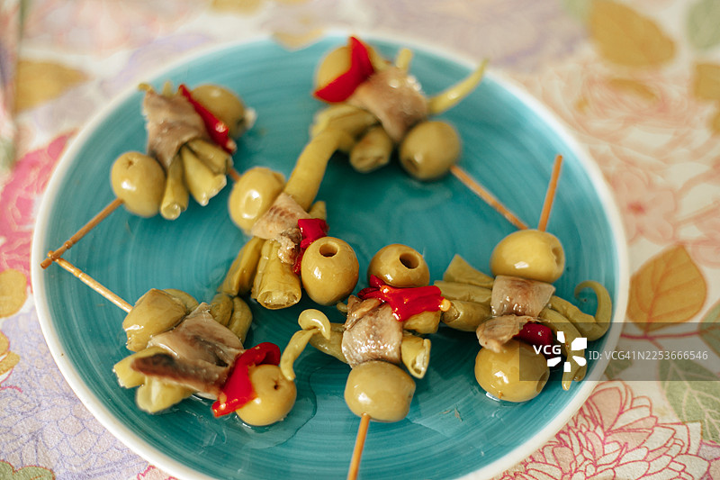 一盘传统的西班牙吉尔达斯，一种经典的西班牙小吃，由绿橄榄、凤尾鱼和腌制的吉达辣椒制成，通常用牙签串起来。图片素材