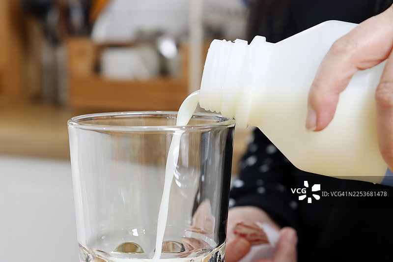 一位女性在明亮的厨房环境中将牛奶倒入玻璃杯中，用于日常营养的概念图片素材